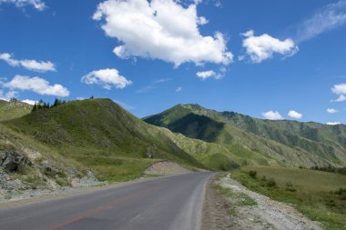 Bulutları ve otoyolu olan mavi gökyüzünün arka planındaki dağ zirveleri