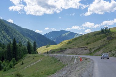 Bulutları ve otoyolu olan mavi gökyüzünün arka planındaki dağ zirveleri