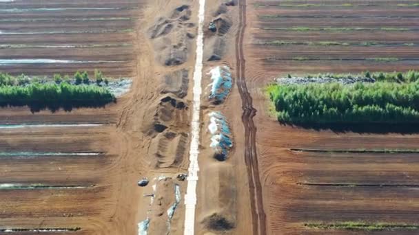 Disparo aéreo volando a lo largo de la carretera sobre el campo de cosecha de turba. Extracción de turba. Montones de turba. — Vídeos de Stock