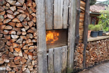 Side view of stacked pile of split firewood and smokehouse