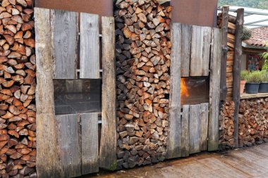 Side view of stacked pile of split firewood and smokehouse