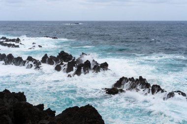 Waves crashing against black rocks in Porto Moniz in Madeira, Portugal