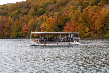 Hırvatistan - 10.19.2025: Hırvatistan 'ın Plitvice Gölleri Ulusal Parkı' nda canlı sonbahar ormanlarıyla çevrili bir göl boyunca seyahat eden turist botu