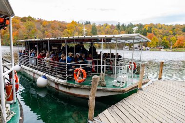 Hırvatistan - 10.19.2025: Hırvatistan 'ın Plitvice Gölleri Ulusal Parkı' nda canlı sonbahar ormanlarıyla çevrili bir göl boyunca seyahat eden turist botu
