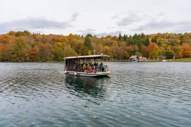 Hırvatistan - 10.19.2025: Hırvatistan 'ın Plitvice Gölleri Ulusal Parkı' nda canlı sonbahar ormanlarıyla çevrili bir göl boyunca seyahat eden turist botu