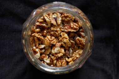 Koyu arkaplanda cam bir kavanozda ceviz yarımları