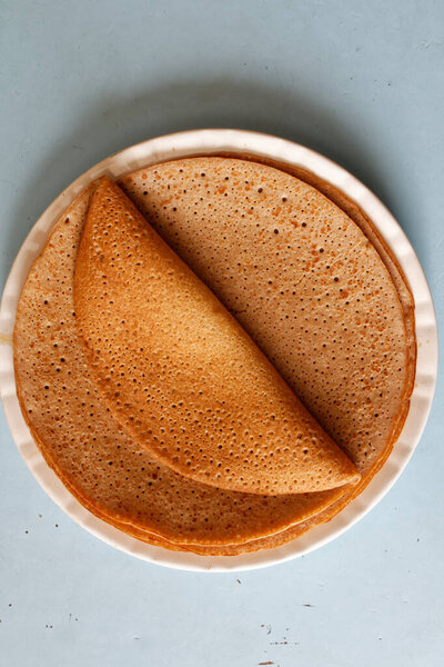 Блинчики, сложенные на большой тарелке на голубом столе.