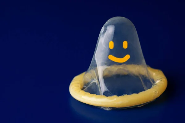 Preservativo amarelo no fundo azul escuro fechar com emoticon alegre — Fotografia de Stock