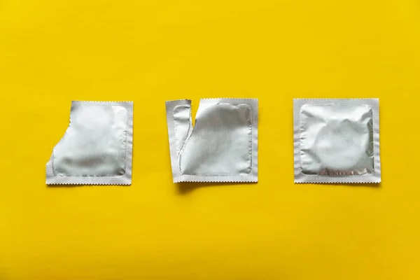 Preservativo e dois pacotes em branco no fundo amarelo — Fotografia de Stock