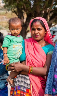 NOIDA, UTTAR PRADESH, INDIA - Kasım 2020: Çocuğuyla birlikte Sari 'deki açık alanda duran köy bölgesinden Hintli bir kadının portresi. Eğitim için okulda çocuklarına bakıyor..