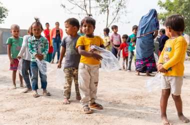 NOIDA, UTTAR PRADESH, INDIA - NOVEMBER 2020: Hindistan 'da Corona salgını sırasında gönüllülerin dağıttığı yiyecekleri toplamak için kenar mahalle veya köy bölgesinden gelen genç çocuklar veya öğrenciler. Topluma geri vermek..