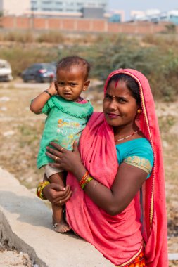 NOIDA, UTTAR PRADESH, INDIA - Kasım 2020: Çocuğuyla birlikte Sari 'deki açık alanda duran köy bölgesinden Hintli bir kadının portresi. Eğitim için okulda çocuklarına bakıyor..