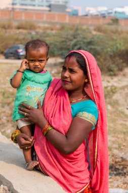 NOIDA, UTTAR PRADESH, INDIA - Kasım 2020: Çocuğuyla birlikte Sari 'deki açık alanda duran köy bölgesinden Hintli bir kadının portresi. Eğitim için okulda çocuklarına bakıyor..