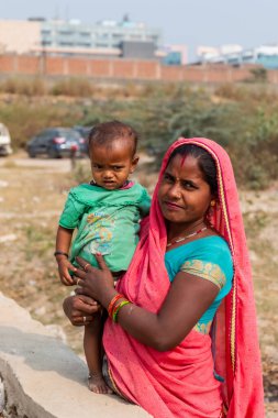 NOIDA, UTTAR PRADESH, INDIA - Kasım 2020: Çocuğuyla birlikte Sari 'deki açık alanda duran köy bölgesinden Hintli bir kadının portresi. Eğitim için okulda çocuklarına bakıyor..