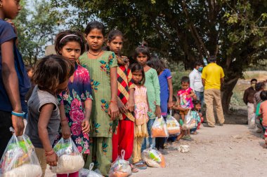 NOIDA, UTTAR PRADESH, INDIA - NOVEMBER 2020: Hindistan 'da Corona salgını sırasında gönüllülerin dağıttığı yiyecekleri toplamak için kenar mahalle veya köy bölgesinden gelen genç çocuklar veya öğrenciler. Topluma geri vermek..