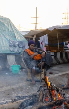 NEW DELHI, INDIA - HAZİRAN 2021: Hint Sih çiftçisi yeni çiftlik yasasına karşı protesto sırasında kamp ateşinin yanında oturuyor. Hindistan 'ın dört bir yanından çiftçiler yeni tarım yasasını protesto ediyorlar..
