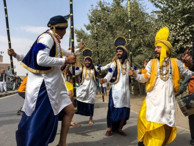 BİKANER, RAJASTHAN, INDIA - HAZİRAN 2019: Sih erkek sanatçı grubu Bikaner şehrindeki sokaklarda renkli sarı ve mavi elbiseler içinde Punjabi Bhangra dansı yapıyorlar.