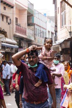 VRINDAVAN, UTTAR PRADESH, INDIA - AĞUSTOS 2021: Krishna Janmashtami, Vrindavan sokaklarında yürürken kızını omuzunda taşıyan Hintli adamın portresi.