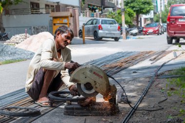 VRINDAVAN, UTTAR PRADESH, INDIA - AĞUSTOS 2021: Krishna Janmashtami, Vrindavan caddesinde oturan ve çeliği dairesel testereyle kesen Hintli adam portresi