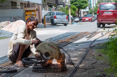 VRINDAVAN, UTTAR PRADESH, INDIA - AĞUSTOS 2021: Krishna Janmashtami, Vrindavan caddesinde oturan ve çeliği dairesel testereyle kesen Hintli adam portresi