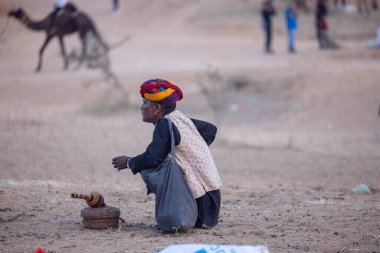 Puşkar, Rajasthan, Hindistan - 10 Kasım 2024: Geleneksel beyaz giysili rajasthani erkek portresi çöl panayırında renkli türbanla deve pazarında develeri takas ederken.