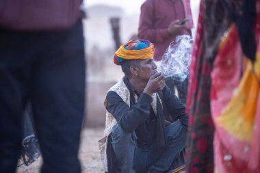 Puşkar, Rajasthan, Hindistan - 10 Kasım 2024: İtme kar deve fuarı sırasında açık zeminde renkli türbanlı kobra yılanı tutan genç yılan oynatıcısı erkek portresi.