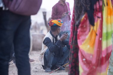 Puşkar, Rajasthan, Hindistan - 10 Kasım 2024: İtme kar deve fuarı sırasında açık zeminde renkli türbanlı kobra yılanı tutan genç yılan oynatıcısı erkek portresi.