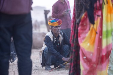 Puşkar, Rajasthan, Hindistan - 10 Kasım 2024: İtme kar deve fuarı sırasında açık zeminde renkli türbanlı kobra yılanı tutan genç yılan oynatıcısı erkek portresi.