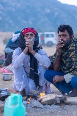 Puşkar, Rajasthan, Hindistan - 11 Kasım 2024: Geleneksel beyaz giysili rajasthani erkek portresi çöl panayırında renkli türbanla deve pazarında deve ticareti yaparken.