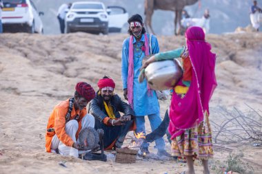 Puşkar, Rajasthan, Hindistan - 11 Kasım 2024: Geleneksel beyaz giysili rajasthani erkek portresi çöl panayırında renkli türbanla deve pazarında deve ticareti yaparken.