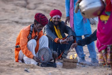 Puşkar, Rajasthan, Hindistan - 11 Kasım 2024: Geleneksel beyaz giysili rajasthani erkek portresi çöl panayırında renkli türbanla deve pazarında deve ticareti yaparken.