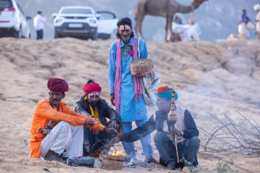 Puşkar, Rajasthan, Hindistan - 11 Kasım 2024: Geleneksel beyaz giysili rajasthani erkek portresi çöl panayırında renkli türbanla deve pazarında deve ticareti yaparken.