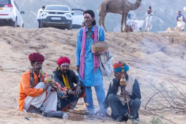 Puşkar, Rajasthan, Hindistan - 11 Kasım 2024: Geleneksel beyaz giysili rajasthani erkek portresi çöl panayırında renkli türbanla deve pazarında deve ticareti yaparken.