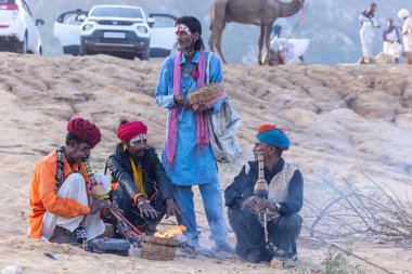 Puşkar, Rajasthan, Hindistan - 11 Kasım 2024: Geleneksel beyaz giysili rajasthani erkek portresi çöl panayırında renkli türbanla deve pazarında deve ticareti yaparken.