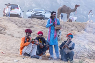 Puşkar, Rajasthan, Hindistan - 11 Kasım 2024: Geleneksel beyaz giysili rajasthani erkek portresi çöl panayırında renkli türbanla deve pazarında deve ticareti yaparken.