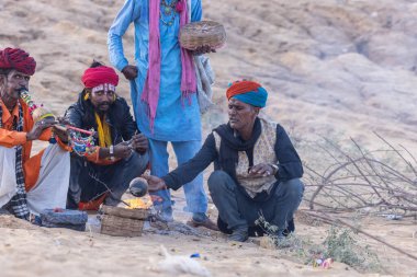 Puşkar, Rajasthan, Hindistan - 11 Kasım 2024: Geleneksel beyaz giysili rajasthani erkek portresi çöl panayırında renkli türbanla deve pazarında deve ticareti yaparken.