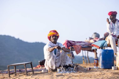 Puşkar, Rajasthan, Hindistan - 11 Kasım 2024: Geleneksel beyaz giysili rajasthani erkek portresi çöl panayırında renkli türbanla deve pazarında deve ticareti yaparken.