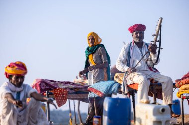 Puşkar, Rajasthan, Hindistan - 11 Kasım 2024: Geleneksel beyaz giysili rajasthani erkek portresi çöl panayırında renkli türbanla deve pazarında deve ticareti yaparken.