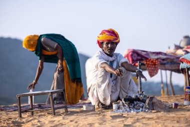 Puşkar, Rajasthan, Hindistan - 11 Kasım 2024: Geleneksel beyaz giysili rajasthani erkek portresi çöl panayırında renkli türbanla deve pazarında deve ticareti yaparken.