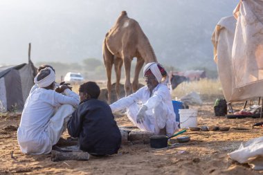Puşkar, Rajasthan, Hindistan - 11 Kasım 2024: Geleneksel beyaz giysili rajasthani erkek portresi çöl panayırında renkli türbanla deve pazarında deve ticareti yaparken.