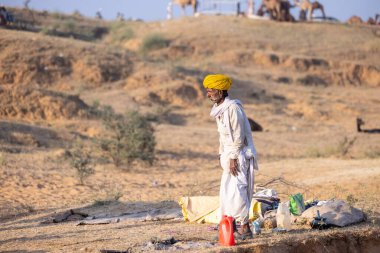 Puşkar, Rajasthan, Hindistan - 11 Kasım 2024: Geleneksel beyaz giysili rajasthani erkek portresi çöl panayırında renkli türbanla deve pazarında deve ticareti yaparken.