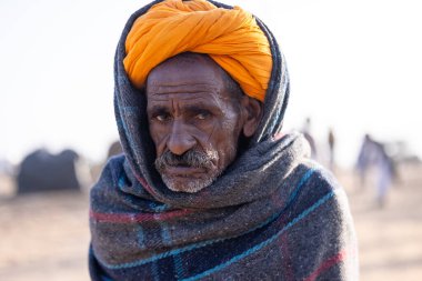 Puşkar, Rajasthan, Hindistan - 11 Kasım 2024: Geleneksel beyaz giysili rajasthani erkek portresi çöl panayırında renkli türbanla deve pazarında deve ticareti yaparken.