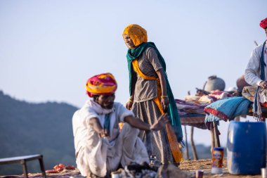 Puşkar, Rajasthan, Hindistan - 11 Kasım 2024: Geleneksel beyaz giysili rajasthani erkek portresi çöl panayırında renkli türbanla deve pazarında deve ticareti yaparken.