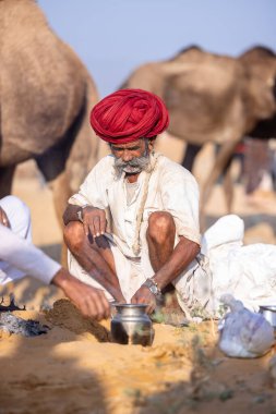 Puşkar, Rajasthan, Hindistan - 11 Kasım 2024: Çöldeki fuar alanında deve ticaret fuarı sırasında renkli türbanlı geleneksel beyaz giysili bir rajasthani erkeğinin portresi.