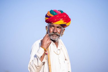 Puşkar, Rajasthan, Hindistan - 11 Kasım 2024: Çöldeki fuar alanında deve ticaret fuarı sırasında renkli türbanlı geleneksel beyaz giysili bir rajasthani erkeğinin portresi.