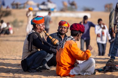 Puşkar, Rajasthan, Hindistan - 11 Kasım 2024: Çöldeki fuar alanında deve ticaret fuarı sırasında renkli türbanlı geleneksel beyaz giysili bir rajasthani erkeğinin portresi. 