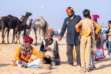 Puşkar, Rajasthan, Hindistan - 11 Kasım 2024: Çöldeki fuar alanında deve ticaret fuarı sırasında renkli türbanlı geleneksel beyaz giysili bir rajasthani erkeğinin portresi. 