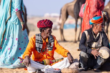 Puşkar, Rajasthan, Hindistan - 11 Kasım 2024: Çöldeki fuar alanında deve ticaret fuarı sırasında renkli türbanlı geleneksel beyaz giysili bir rajasthani erkeğinin portresi. 