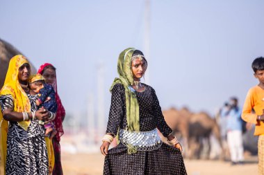 Puşkar, Rajasthan, Hindistan - 11 Kasım 2024: Kimliği belirlenemeyen Hintli Rajasthani kadınlarından oluşan bir grup kış sabahı Pushkar Camel Panayırı 'nda geleneksel renkli elbiseler giyiyor.
