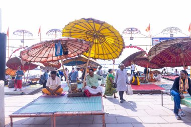 Varanasi, Uttar Pradesh, Hindistan - 22 Mart 2024: Varanasi 'deki çetelerin yakınındaki assi ghat' ta şemsiye altında oturan geleneksel bir Brahman rahibinin portresi.